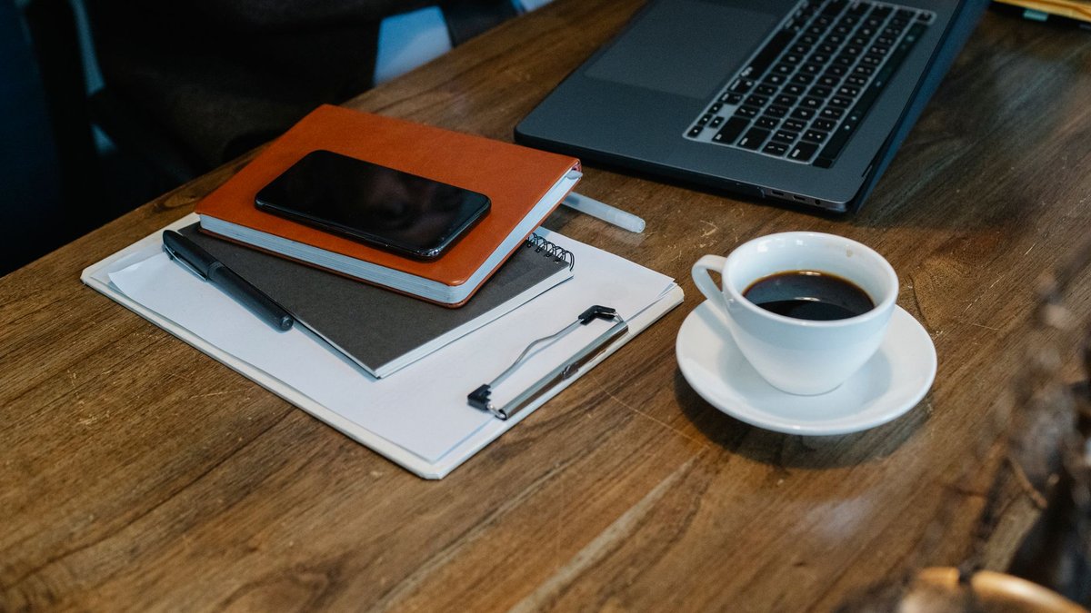 Mesa de trabalho com notebook e bloco de notas, representando a checagem de fontes de uma pesquisa com IA